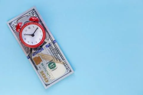 The alarm clock stands on a stack of money on a blue background Stock Photos