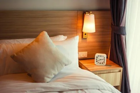 Alarm clock on the table under the lamp near bed. Stock Photos