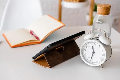 Alarm clock, tablet and notepad on a white table. Workplace in the office. .. Foto stock