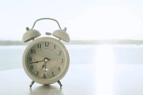 Alarm clock on white table with river and nature background, morning relax ti Stock Photos