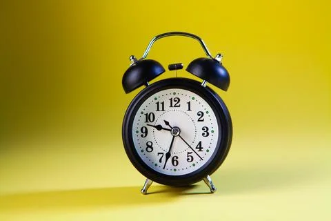 Alarm clock on a yellow background with a shadow. Stock Photos
