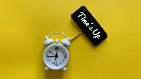 Alarm clock on yellow background with text on small black signage - Time is up. Stock Photos