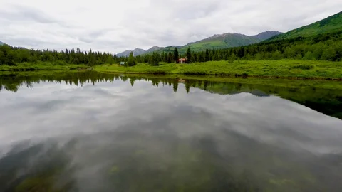 Alaska 4k drone tracking over mirror glass calm lake toward rustic lake cabin Stock Footage 78577300
