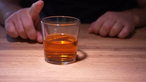 An alcoholic at a table in front of a glass of whiskey tries to resist the urge Stockbeeldmateriaal 342396889