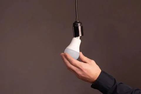 Ale hands screw in an energy-saving LED light bulb. Stock Photos
