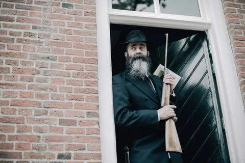 Alert man with long beard standing with rifle in door post. Stock Photos