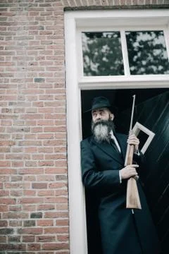 Alert man with long beard standing with rifle in door post. Stock Photos