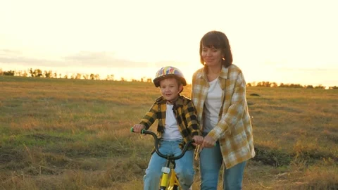 Alert mother provides steady support to exuberant child preventing falls on bike Stock Footage 257347321