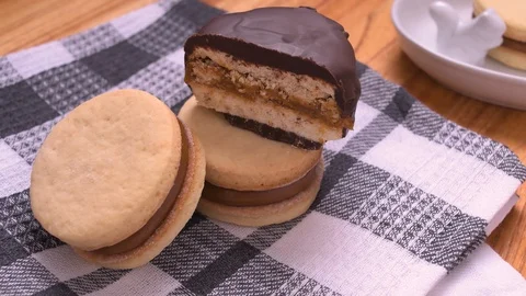 Alfajor Bitten on Half and Dulce de Leche on Gray Kitchen Rag Pan Over Wood Video stock 129351274