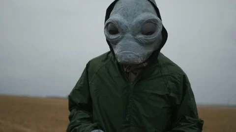 An alien in a green suit stands alone in field, looks around, waves his hand, Stock Footage 145111555