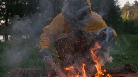 Alien sitting in a yellow suit by fire, evening in nature, UFO concept Stock Footage 142122488
