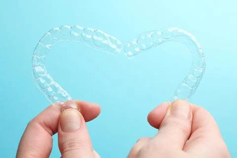 Aligners for aligning teeth on a blue background in a female hand Foto stock
