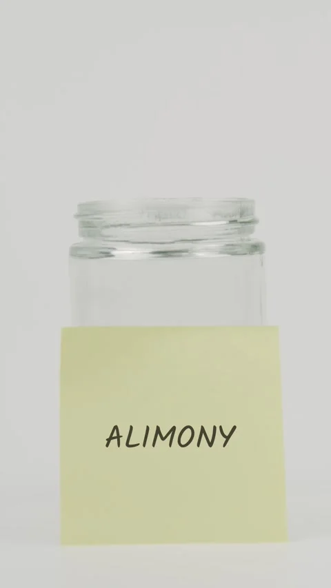 Alimony text or word on yellow sticky note attached to glass jar with hand Stock Footage 311676798