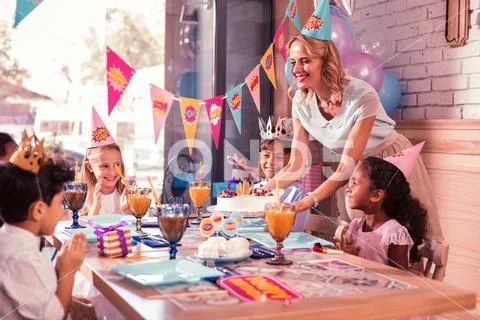 All children smiling while kind mother bringing birthday cake Stock Photos