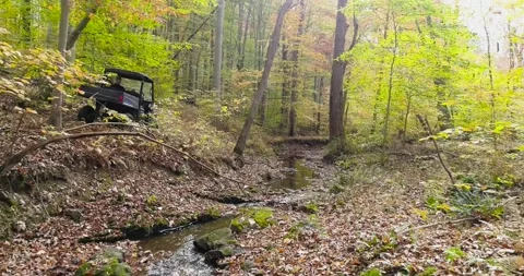 All terrain vehicle navigating down a path along a stream in the forest Stock-Footage 254498519
