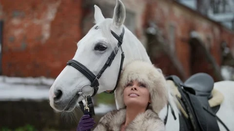 Alluring lady in fur hat and graceful white horse, portrait in equine yard, man Vidéo 179842295