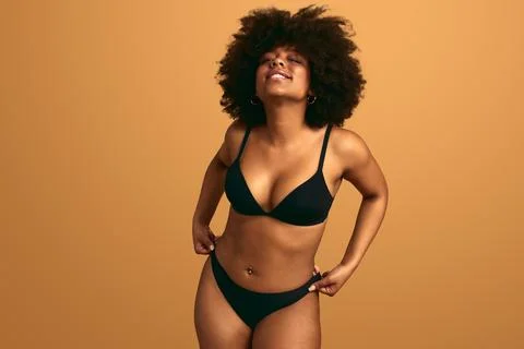 Alluring plus size ethnic lady in underwear smiling at camera in studio Stock Photos