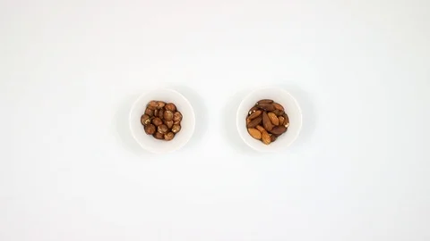 Almonds and hazelnuts in a plate on a white table. The man is eating nuts. Video stock 88399209
