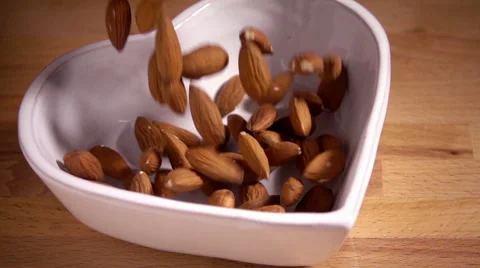 Almonds falling in slow motion into heart shaped bowl Stock Footage 55451943