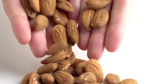 Almonds nuts falling on the white table. Woman holding almonds nuts in hand.. Stock Footage 252056318