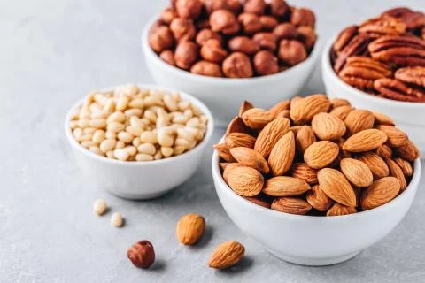 Almonds, pecans, pine nuts and hazelnuts in white bowls on grey background. N Stock Photos