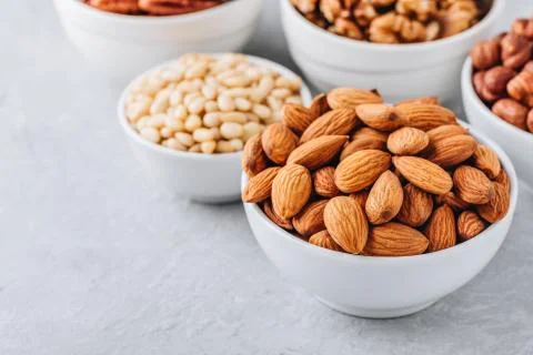 Almonds, pecans, walnuts, pine nuts and hazelnuts in white bowls on grey back Stock Photos