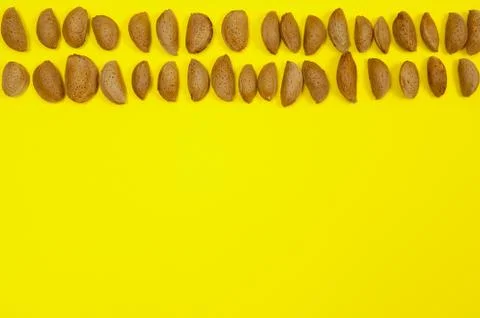 Almonds in two rows on yellow background with copy space Stock Photos