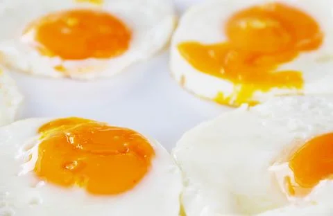 Almost done fried eggs; orage yolk and egg white on the white plate Stock Photos