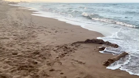 An almost empty beach at sunset with soft waves breaking up a sandcastle Stock Footage 313446529