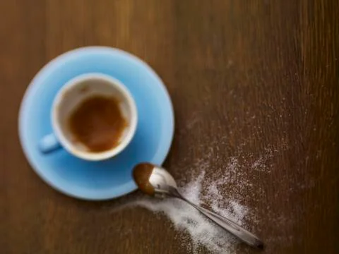 An almost-empty espresso cup and sugar sprinkled next to it Stock Photos
