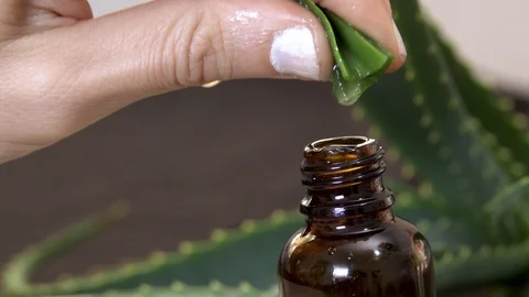 An aloe vera gel drops falling into glass brown battle from plants leaf. Natu Видео 124471047