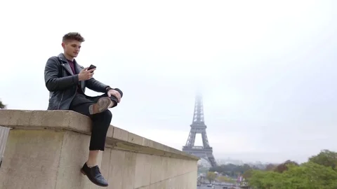 Alone handsome man is sitting on stone wall in Paris in fall day, reading Stock Footage 98811092