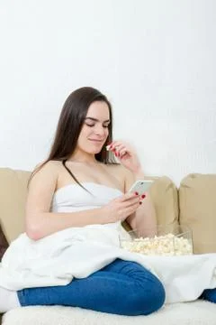 Alone happy female model with cellphonel sitting on bed with blanket Stock Photos