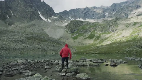Alone hiker man in red jacket is looking around among beautiful mountain lake Stock Footage 137941664