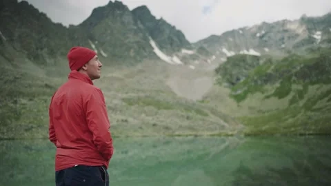 Alone hiker man in red jacket is looking around among the lake and mountains Stock Footage 137941677