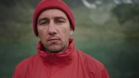 Alone hiker man in red jacket and hat is looking at camera among mountains Stock Footage 137941723