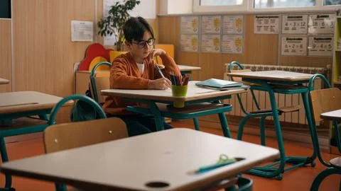 Alone little boy in empty school class room sitting at desk table writing Stock Photos