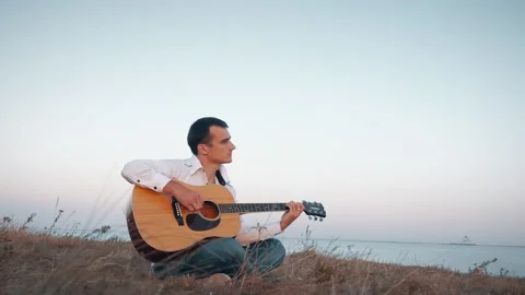 Alone man playing guitar sitting on the coast Stockbeeldmateriaal 161093964
