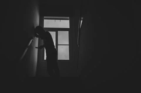 Alone man silhouette standing using phone at the window closed in darkhome. Stock Photos