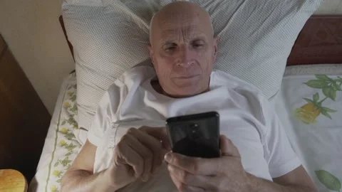 Alone older grandfather lying in bed and looking to smart phone. Stock Footage 170947853