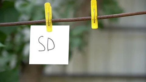 Alone paper with word SD on yellow clothespin hanging on rod near empty pin. Stock Footage 108775058