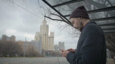 Alone young man on bus stop listening music in ear phones Stock Footage 90254897