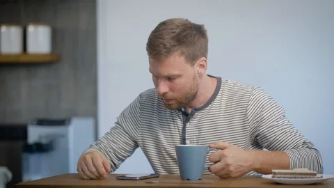 Alone young man is having breakfast in his apartment, sitting on kitchen Video stock 93849751