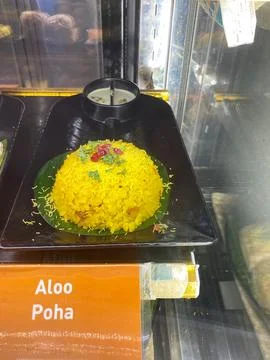 Aloo Poha dish displayed in a cafe, featuring yellow flattened rice garnished Stock Photos