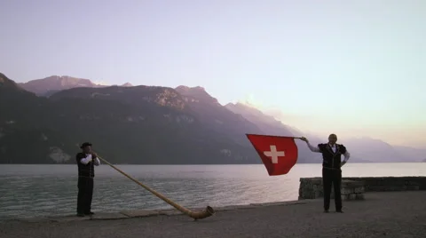 Alphorn player and flag thrower perform near lake Vidéo 52233725