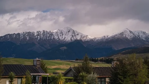 Alpine houses and fields of grass with storm clouds over mountains New Zealand Stock Footage 120123656
