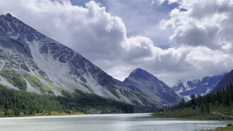 Alpine lake nestled between snow capped mountain peaks, coniferous forest Video stock 347349393