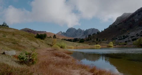 Alpine lake reflecting the cloudy sky in autumn. The surrounding hills and Stock Footage 337128413