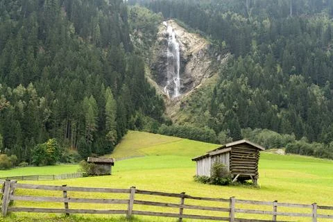 Alpine Meadow with Rustic Barns and a Waterfall in the Background Stock Photos