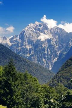 Alpine mountain peak with few clouds surrounded by coniferous forests Foto stock